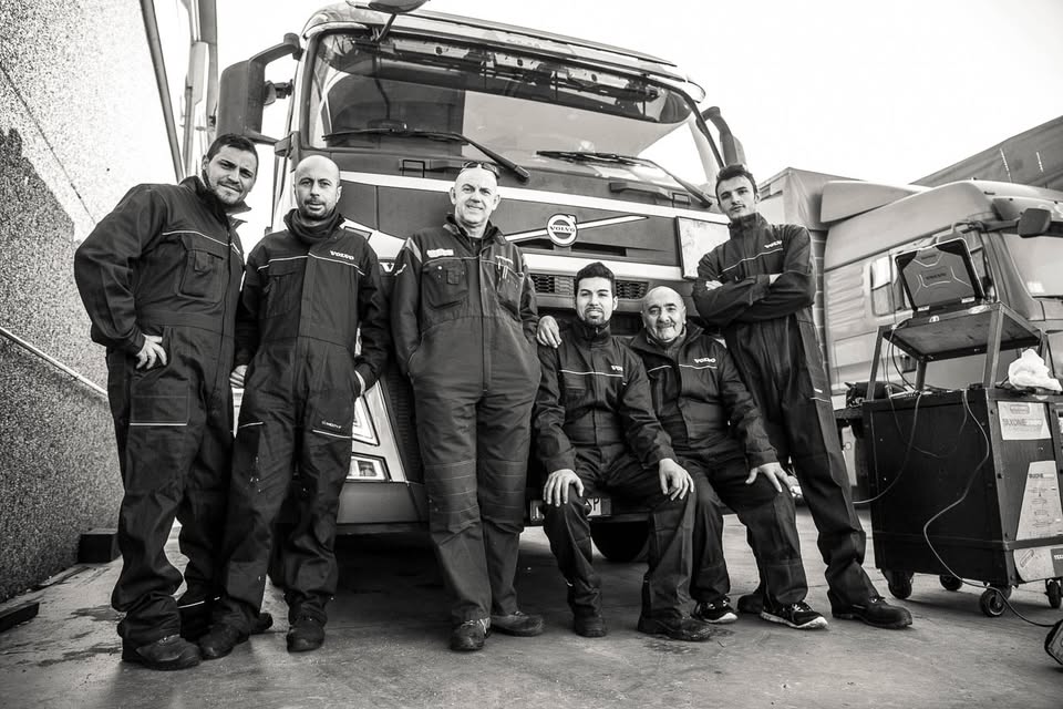 Squadra di meccanici Scudiero in tuta da lavoro davanti a un camion Volvo, accanto a un carrello diagnostico, in bianco e nero