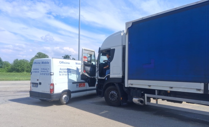 Furgone bianco Officina Mobile Assistenza Multimarche accanto a camion con telone blu e autista in cabina su piazzale